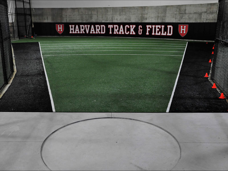 Black and green sport turf inside Harvard Track and Field training facility with orange cones