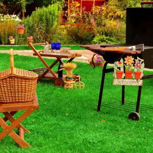 BBQ grill and tables adorned with picnic decor with bright green grass and foliage