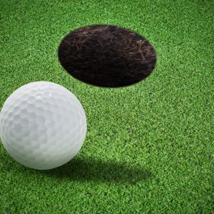 Close-up view of a golf ball near a putting hole on short artificial putting turf