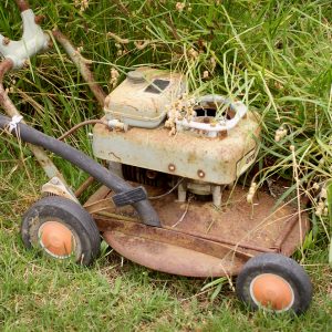Old rusty lawn mower being pushed against long grass on left side and short grass on right