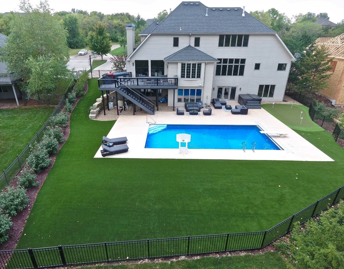 The back of a large house with an artificial grass lawn and pool.